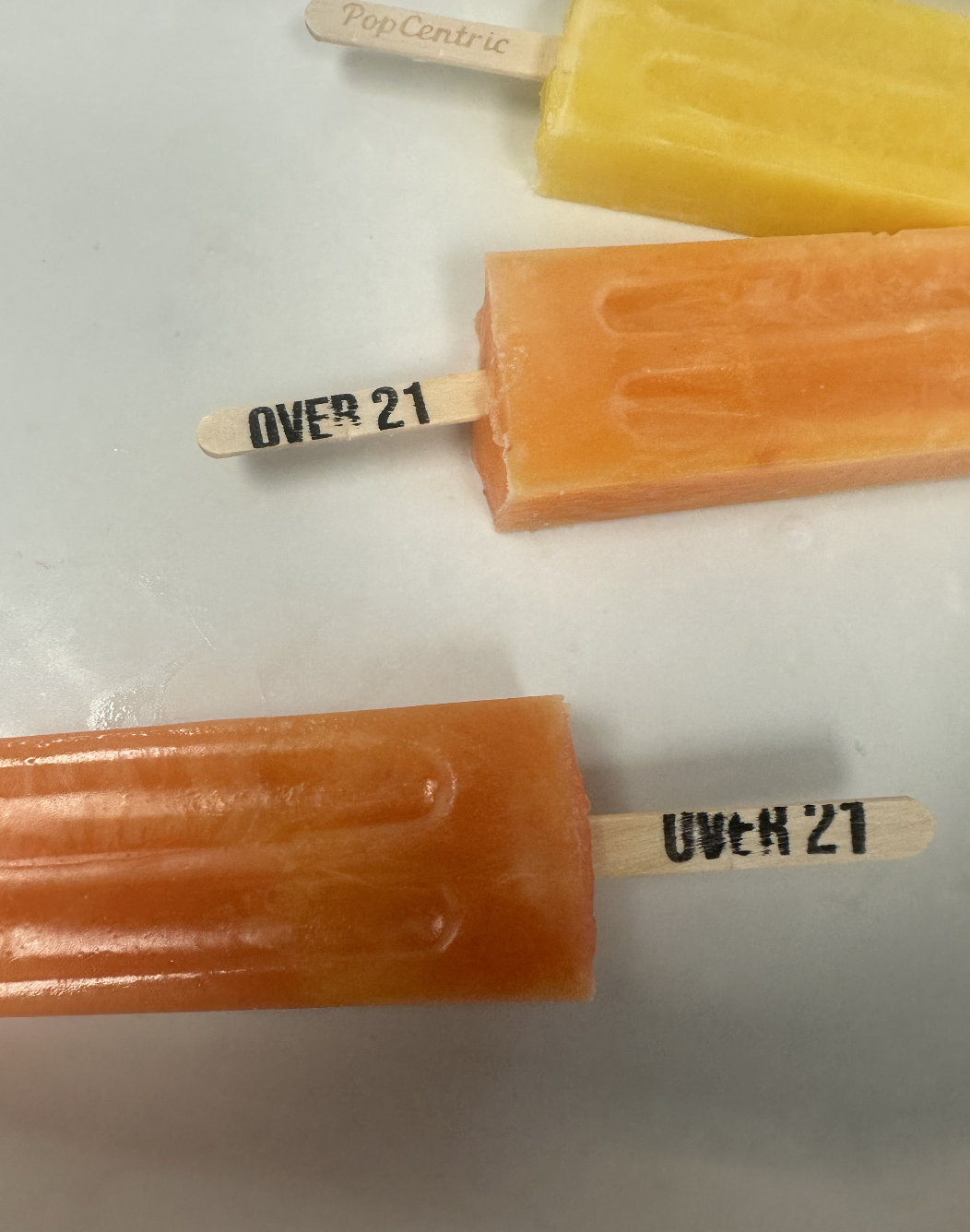PopCentric boozy pops with Over 21 branded sticks next to a classic lemon pop